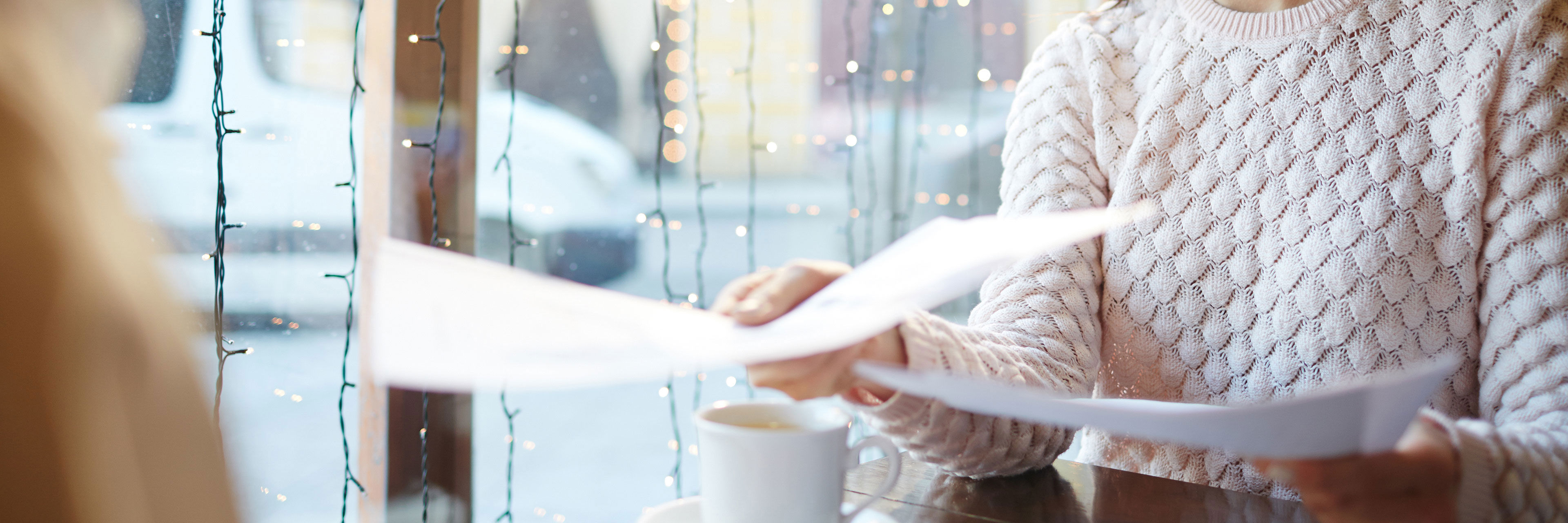 Smilende kvinde der rækker papirer over et bord
